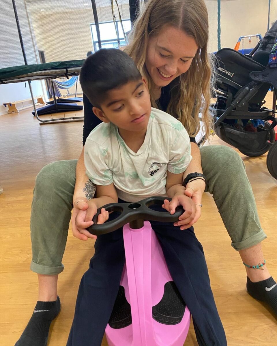 A small child is riding on a pink scooter with an adult helping behind