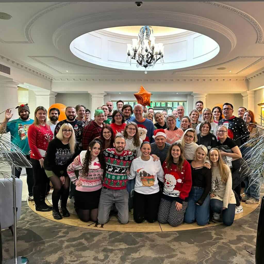 The image is of a large group of people all in festive attire, in a grand hall all smiling into the camera.