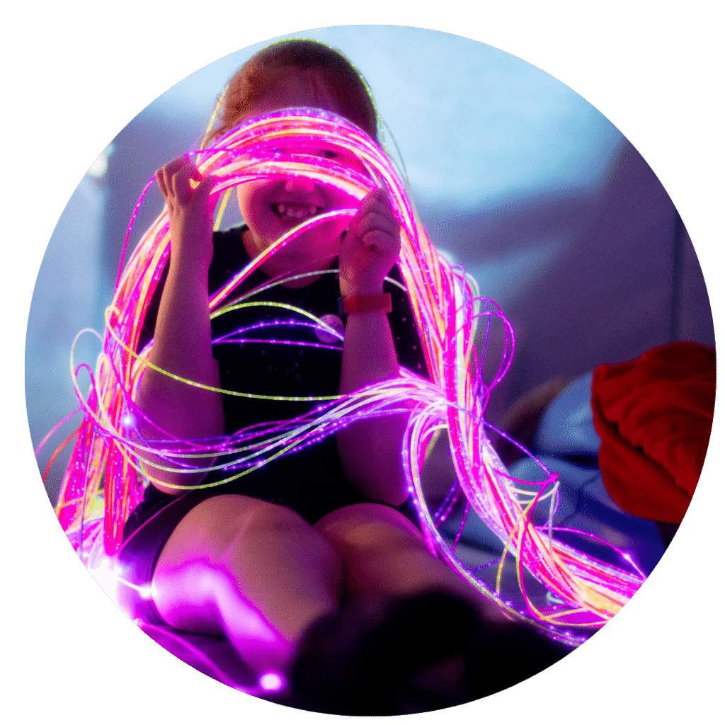 A young child looking through the colourful fibreoptic lights and smiling at Gympanzees sensory room