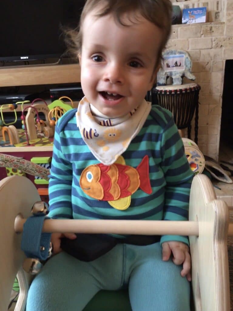 A child sitting in a supportive rocking horse smiling