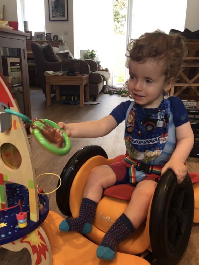 A child in a supportive wheelchair car playing with toys.