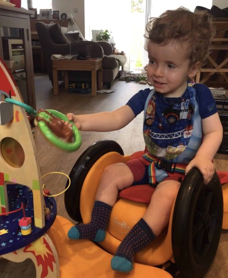 A child in a supportive wheelchair car playing with toys.