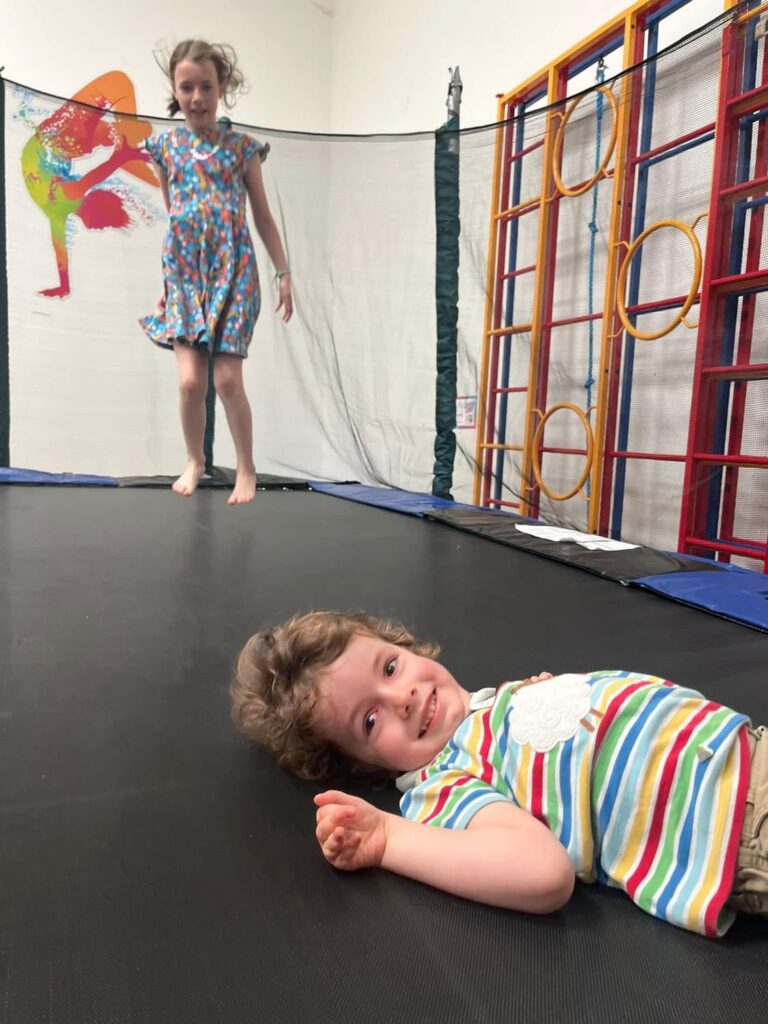 Two children on a trampoline. One is bouncing another one