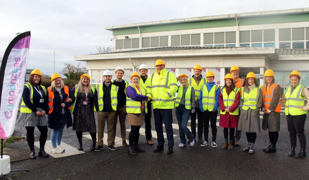 A snapshot of Oakland Construction and Gympanzees teams in hard hats and safety vests, standing outside a commercial building.