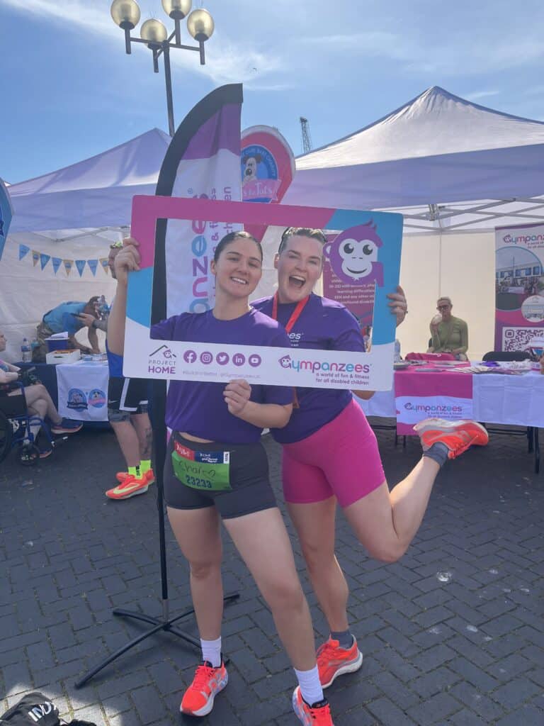 The image is of two runners posing for a photo holding up a selfie frame and flag behind all with Gympanzees branding attached.