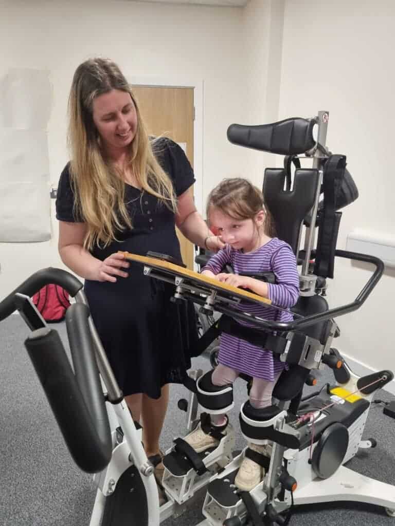 The circular image is of a woman with a small child, assisting with the child in an Innowalk piece of kit. A piece of equipment helped to aid those with less mobility to be able to stand and simulate walking.