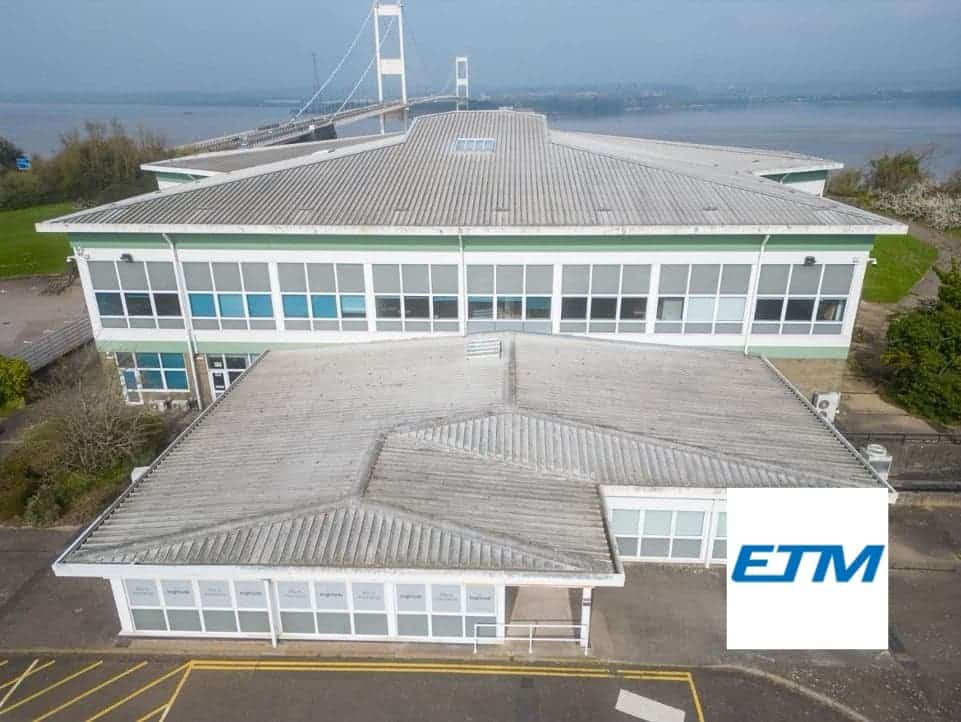 The image is of a front facing view of a large scale wide, lightly colour building with a bridge and water in the background. In the bottom right corner there is a light square with the logo in bold letters, 'ETM.'