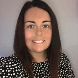 This circular image is of a woman from the shoulders up in a patterned dark top. She has dark, mid-length hair, smiling into the camera on a slightly dark background.
