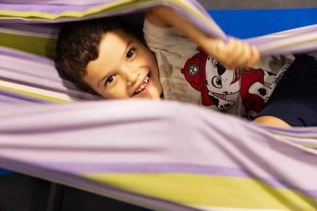 This image is of a child led sideways, in a hammock smiling into the camera.