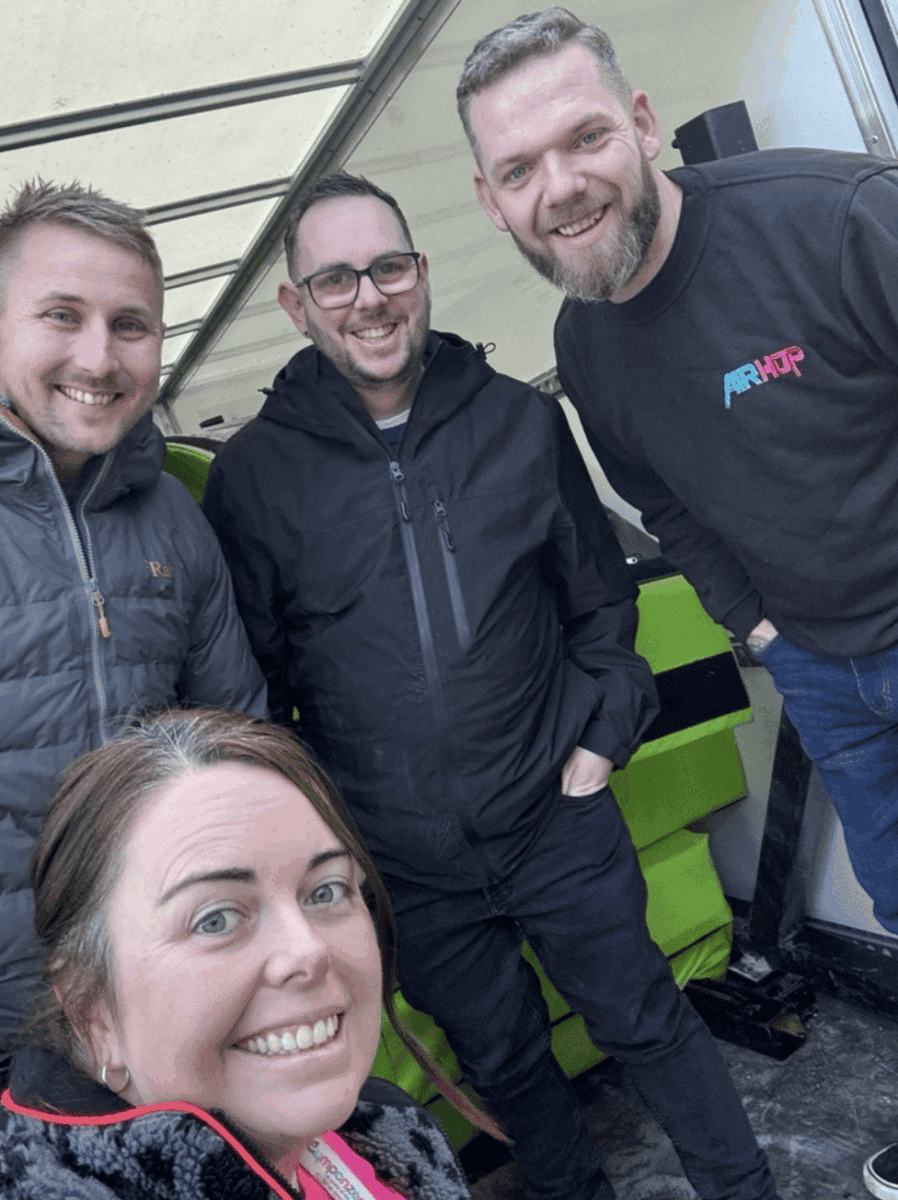 The image is of four people smiling into the camera stood in front the inside of a large truck, with one jumper with the logo, 'AirHop'.