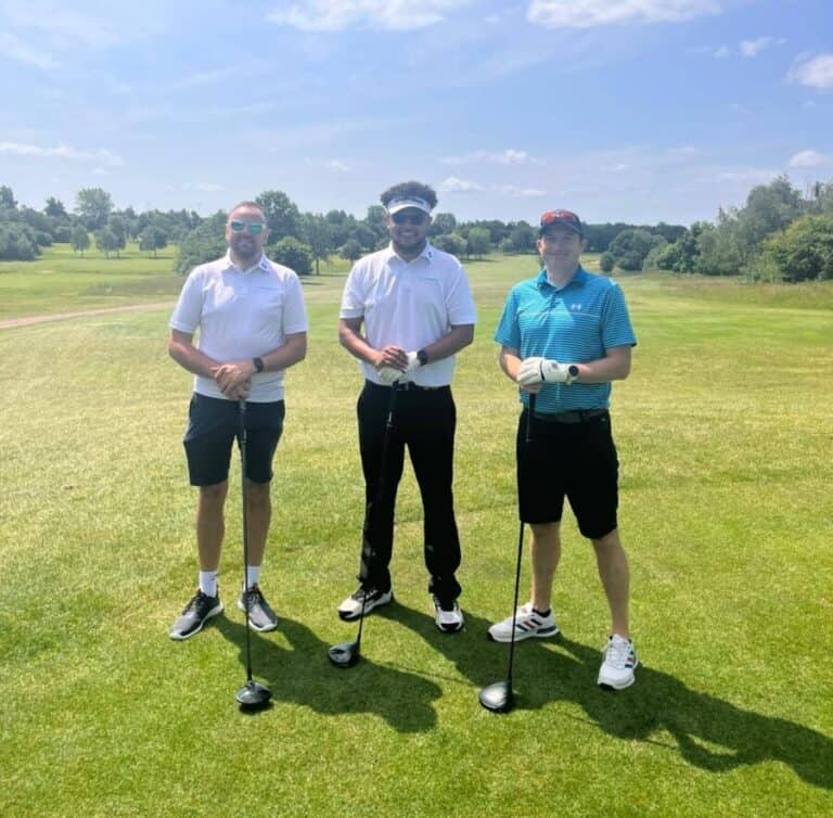 The image is of 3 men, stood facing the camera, in sports wear, all holding golf clubs, on a grasy and sunny backdrop.