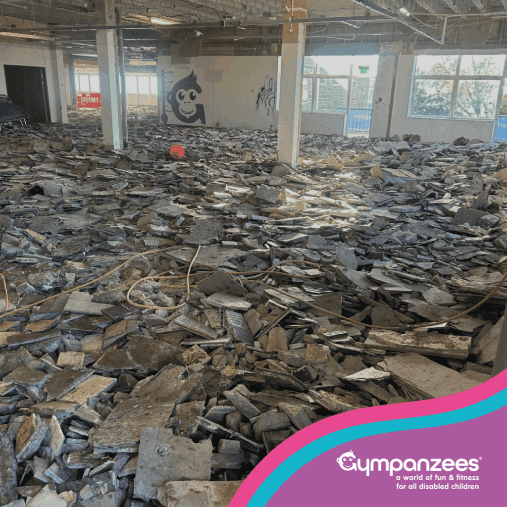 Interior of a building under demolition or renovation, featuring debris and broken tiles on the floor. A Gympanzees logo is visible on a wall, and a sign for "Gympanzees" is in the lower right corner.