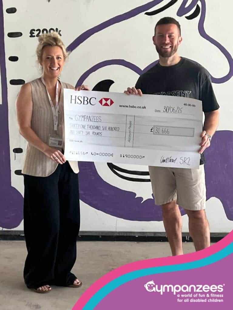 The image is of two people smiling holding a cheque. The photo is framed, with Gympanzees branding on a construction site background.