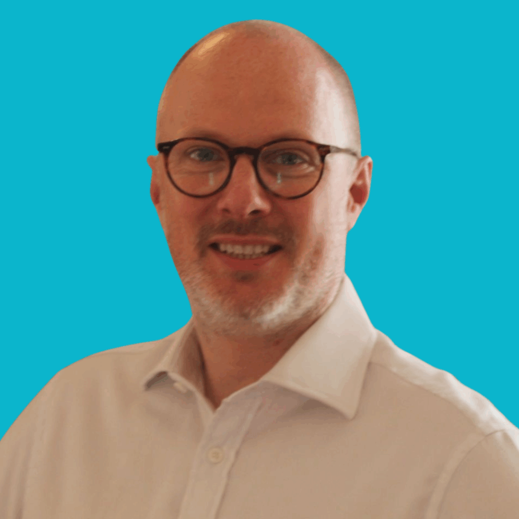 The image is of a man with glasses in a white shirt from the shoulders up, on a bright background smiling into the camera.