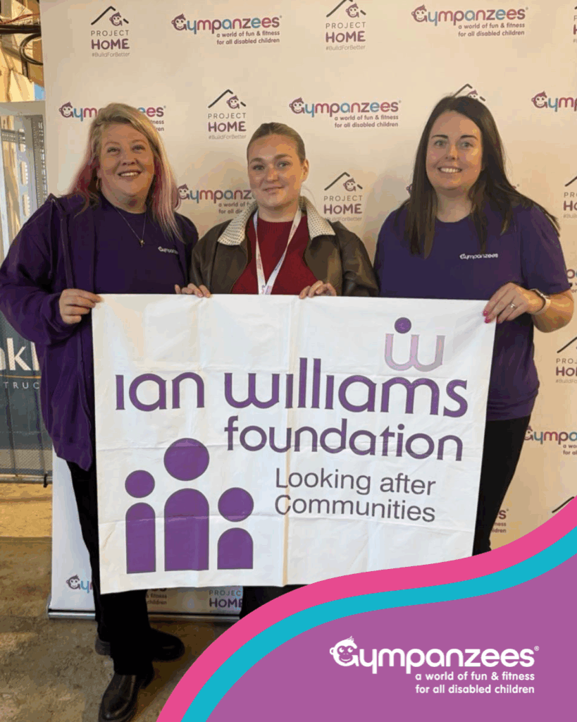 Three people stand smiling in front of an Ian Williams Foundation banner, holding a sign that says, “Looking after Communities.” They wear branded clothing, with the Gympanzees and Project Home Appeal logos visible in the background.