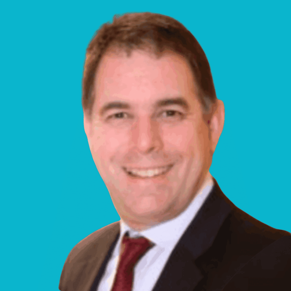 The image is of a man with short hair, from the shoulders up, in a suit and tie, smiling with a bright background.