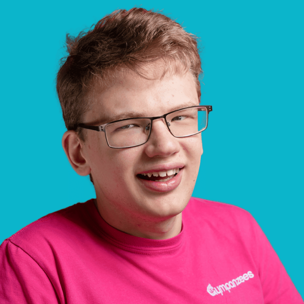 The image is of a young man, from the shoulders up, in a brightly coloured shirt, short hair and glasses, smiling into the camera on a bright background.