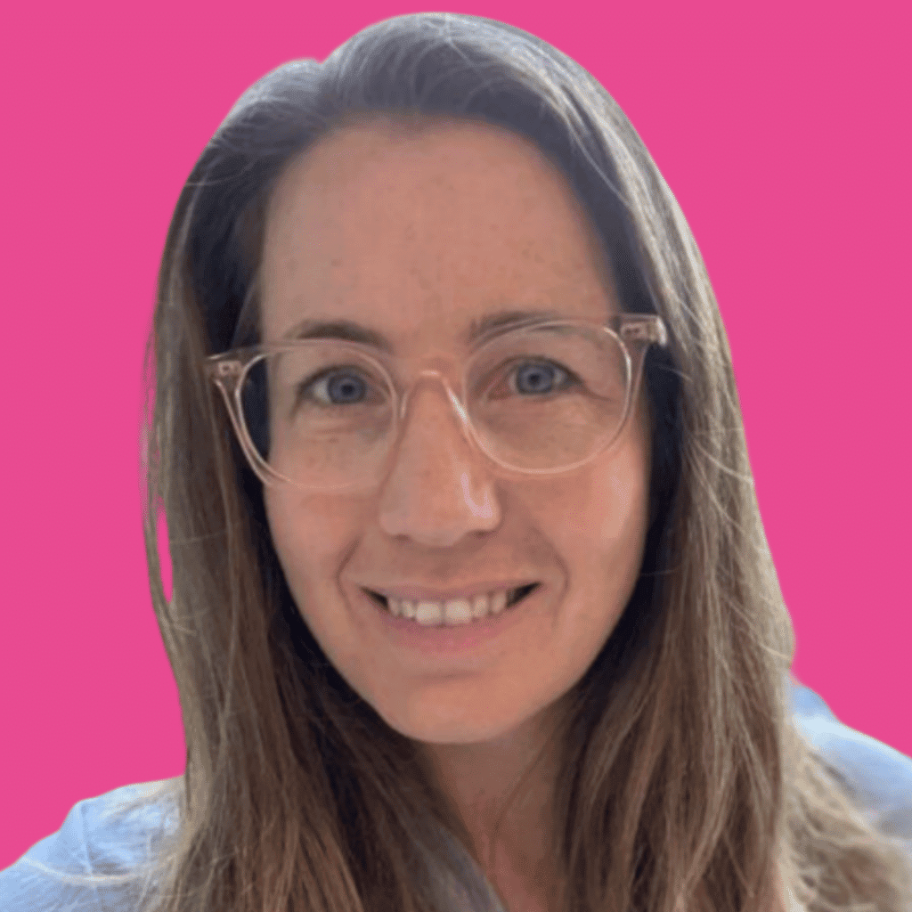The image is of a lady with light long hair and glasses from the shoulders up smiling into the camera, with a bright background.