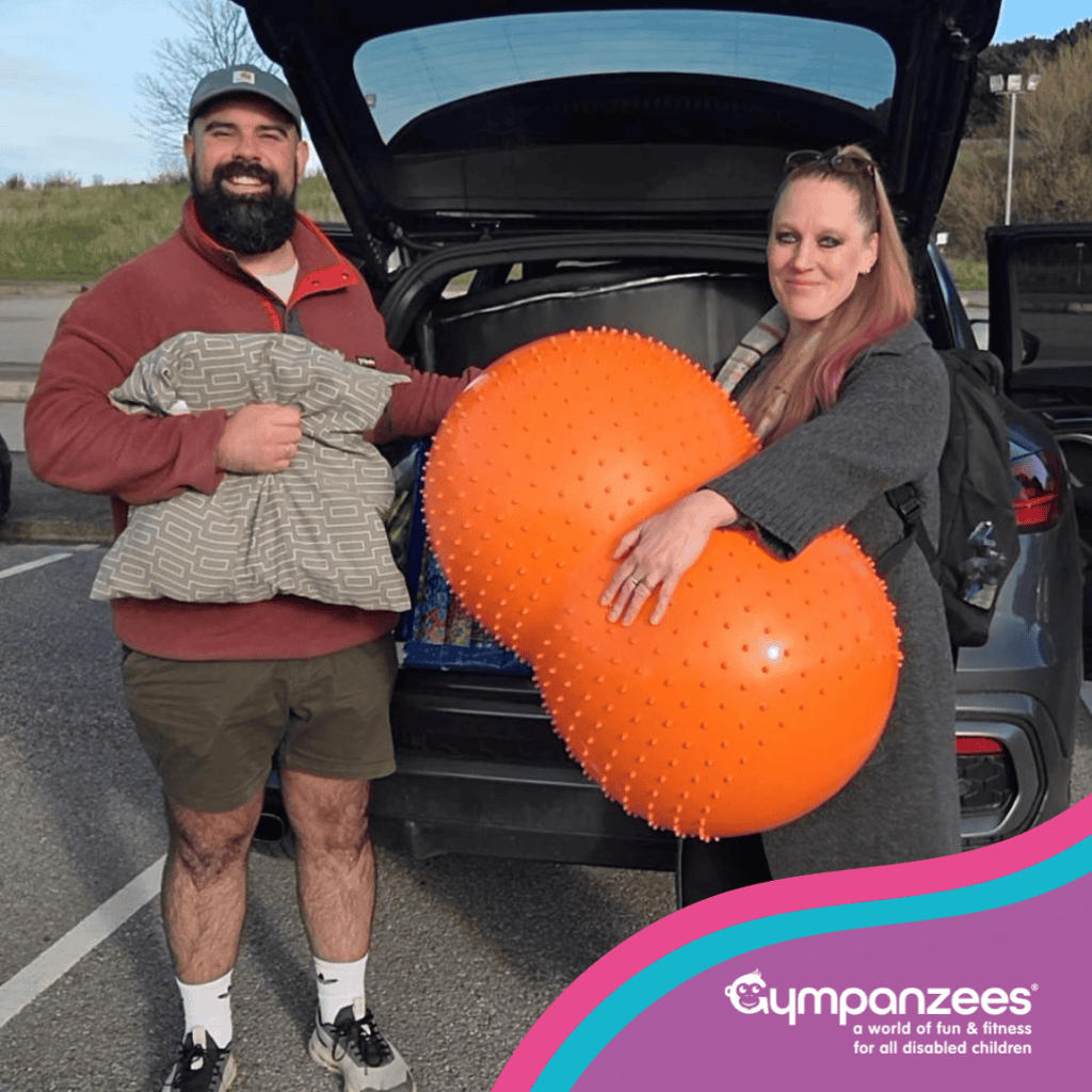 Two people posing for a photo with Lending Library equipment in front of an open car boot
