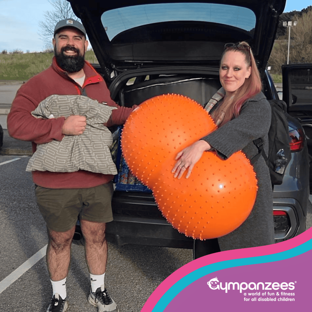 Two people posing for a photo with Lending Library equipment in front of an open car boot