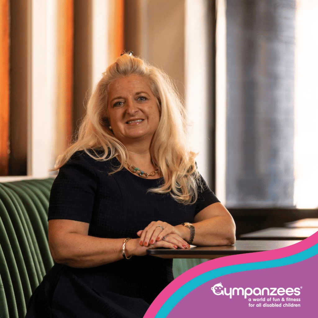 A smiling woman from the Gympanzees Commercial Property Committee leaning on a table in a modern indoor space, with Gympanzees branding in the corner.