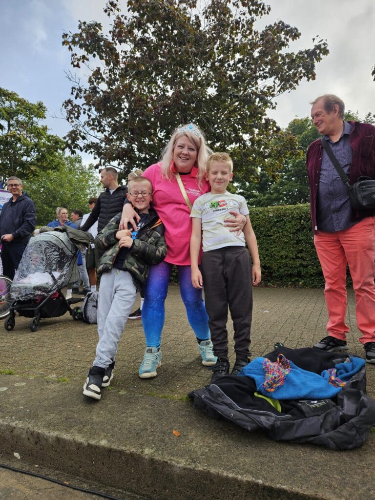 The image is of three individuals in brightly coloured tops huddled together smiling into the camera with a tree in the background.