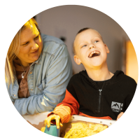 The image is of a woman looking at her son next to her, who is smiling towards someone off camera, leant over a lit up sandpit.