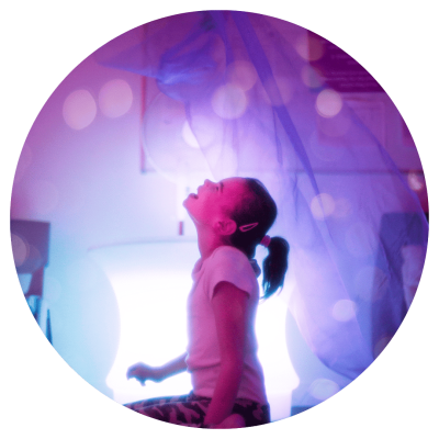 A young child in a dark sensory room with lights and colourful cloths.