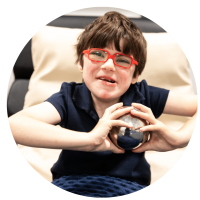 A young child smiling for the camera playing with metal sensory ball.