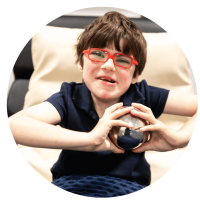 A young child smiling for the camera playing with metal sensory ball.