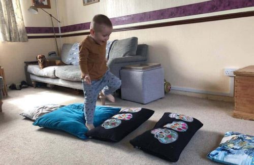 The image is of a small child stepping across various pillow laid out on the floor in front of him in a living room.