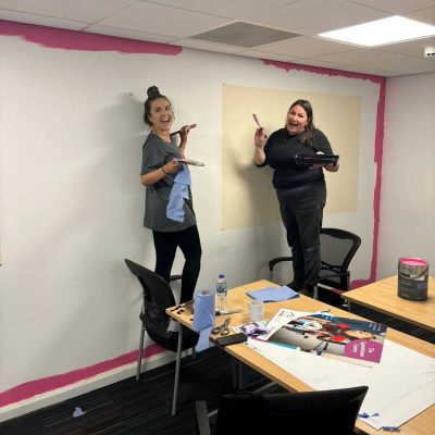 Two individuals stood on chairs painting the walls.