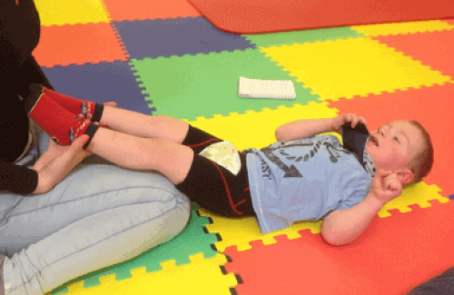 The image is of a little boy, with his legs being held up, being assisted with adapted floor workouts for cerebral palsy.