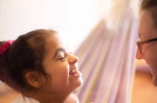 Image is of a young girl smiling at a lady holding her hand whilst sat in a hammock.