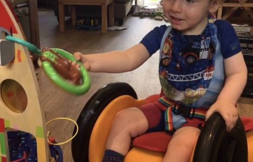 A child in a supportive wheelchair car playing with toys.