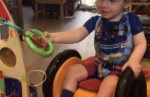 A child in a supportive wheelchair car playing with toys.