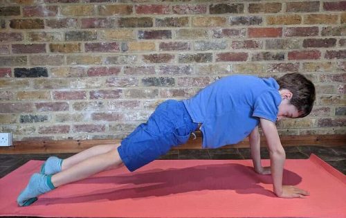 An image from the side of a young boy in a plank position on an exercise mat.