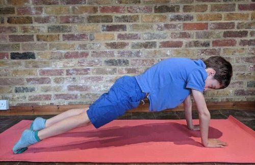 An image from the side of a young boy in a plank position on an exercise mat.