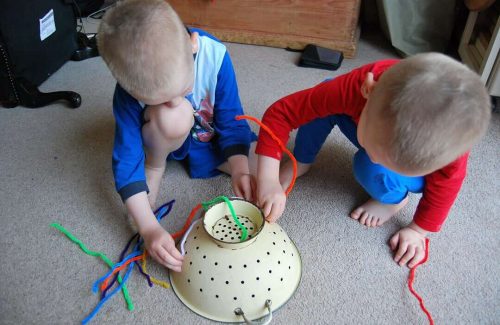 An image of two young boys leaning over an upside down colliander, threading in colourful pipe cleaners into the holes.