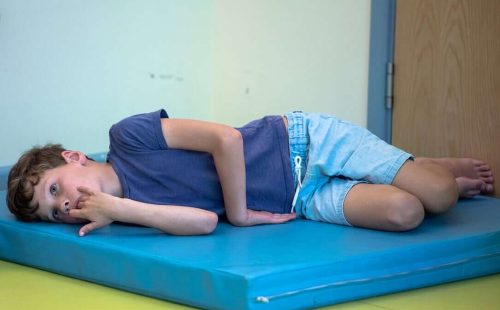 An image of a young boy, led down on his side on a thick, brightly coloured mat.