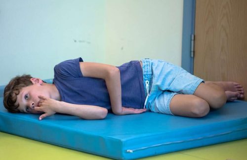An image of a young boy, led down on his side on a thick, brightly coloured mat.