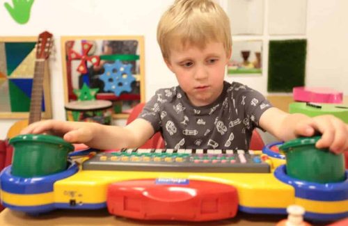 An image of a young boy playing on a colourful toy keyboard, with various instruments in the background.
