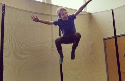 The image is of a young boy sprung in the air with a large trampoline underneath him.
